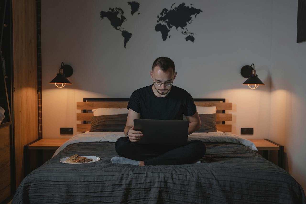 A Man Using a Laptop while Sitting on a Bed